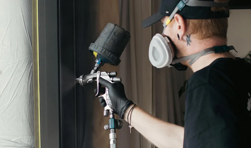 Professional spray painter applying a smooth black coating to an aluminium window frame using a spray gun during the aluminium joinery recolouring process.