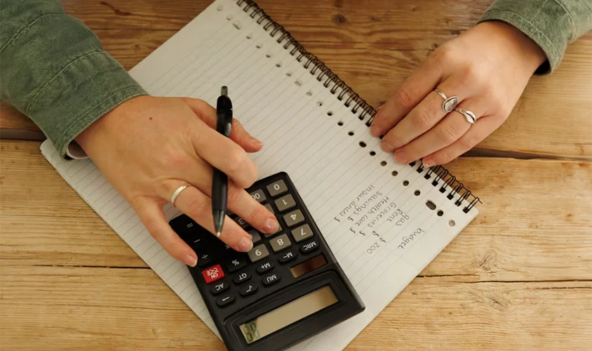 Person using a calculator and notebook to estimate the cost of aluminium joinery recolouring with Nano-Clear compared to window replacement in New Zealand.